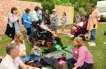 Image shows a group of different people of different ages, some standing up, some sitting down, some in wheelchairs.