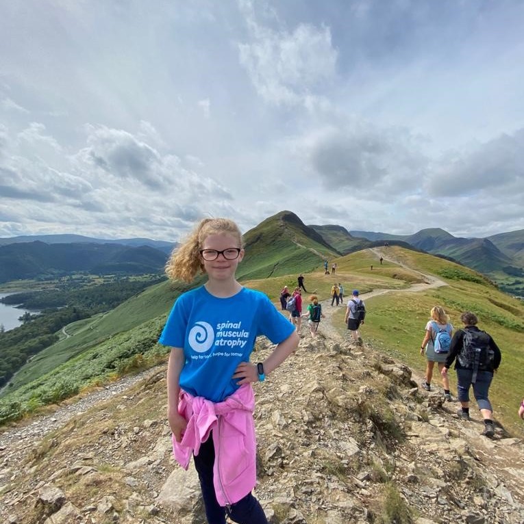 Girl in SMA UK T-shirt at the top of a mountain