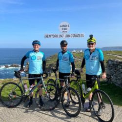 Three cyclists in SMA UK tops at the Lands End sign