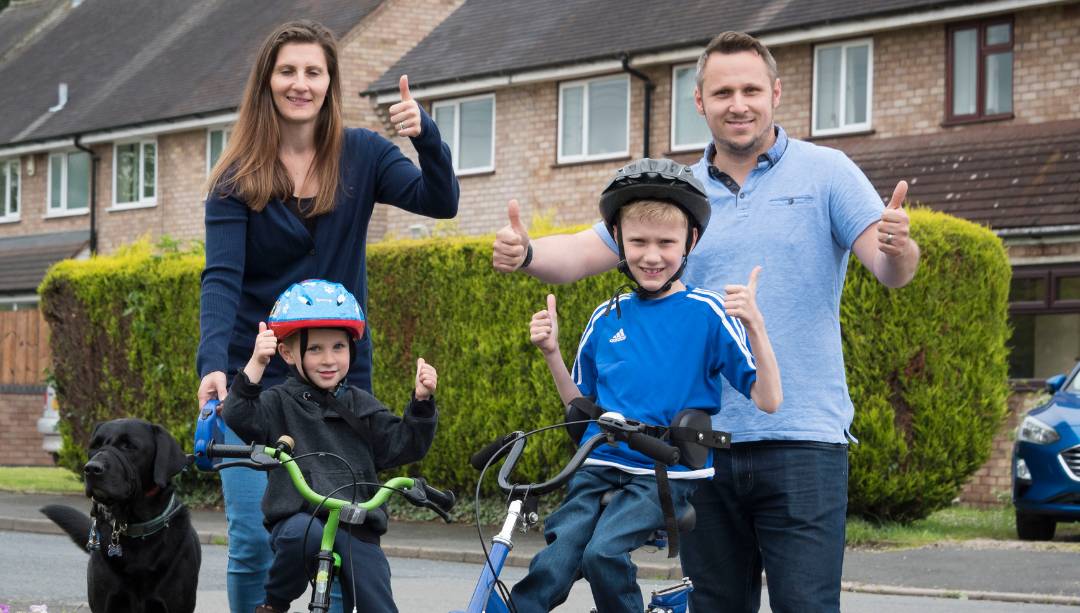 Family of four with two boys riding bikes, one boy has SMA Type 3 and is riding an adapted trike