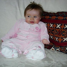 Infant in pink babygrow sat on sofa