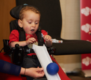 Image shows a young boy with SMA Type 2 playing boccia.