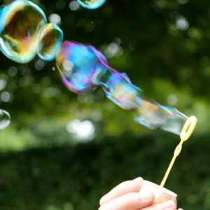 Image shows a hand and bubbles being blown through a bubble wand.