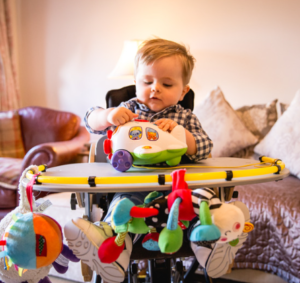 Image shows a young child with SMA Type 2 in a highchair with a tray, playing with toys.