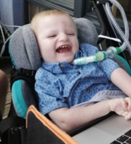 Image shows a young boy who has SMARD. He has a tracheostomy and is wearing a blue t-shirt, he's sitting in supported seating.
