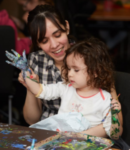 Image shows a mother and her daughter, who has SMA, using paint for messy play.