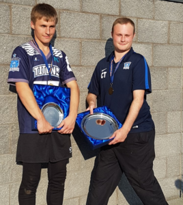 Image shows two teenagers standing next to each wearing sports kit and medals, and both holding silver prizes.