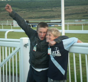 Image shows two young boys smiling and with their arms round each other.