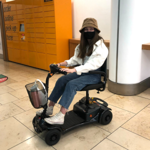 Image shows a young adult who has SMA. She is sitting on a black mobility scooter.