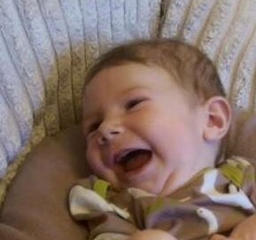 Image shows a baby boy lying on his side and laughing.
