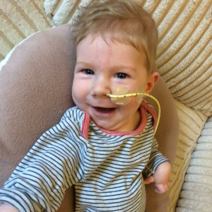 Image shows a baby boy lying on his side and smiling. He's wearing a stripy top.