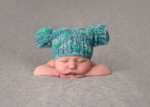 Image shows a baby boy lying down, wearing a blue knitted hat.