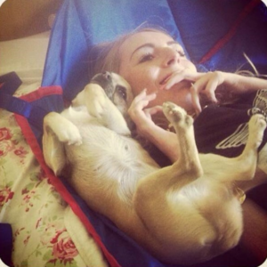 Image shows a young adult woman lying down next to her dog, a chihuahua.