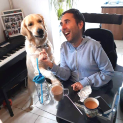 Image shows a man sitting in his wheelchair, with his golden retriever next to him.