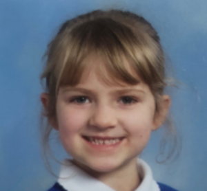 Image shows a young girl with fair hair in a blue school uniform with a white collar.