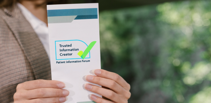 Image shows a woman holding a leaflet with the Patient Information Forum logo on it.