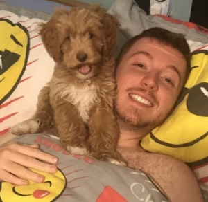 Image shows a man who has SMA, lying in bed. His golden puppy is sitting on his shoulder.