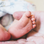 Image shows baby's feet and an adult's hand