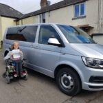 Jordanne next to her wheelchair drive-in van holding her driving certificate