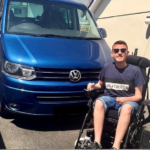 Image shows Ross sitting in his wheelchair next to his blue WAV