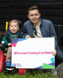 Father Ben and son Ollie hold up a banner saying 'screen today for sma'
